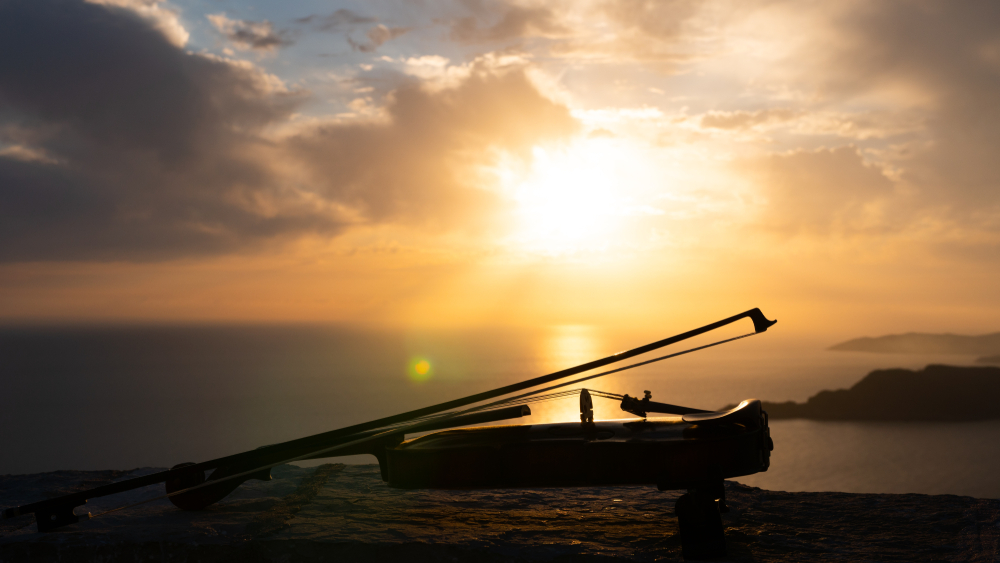 A violin with a bow on top of it, with a sunset behind it